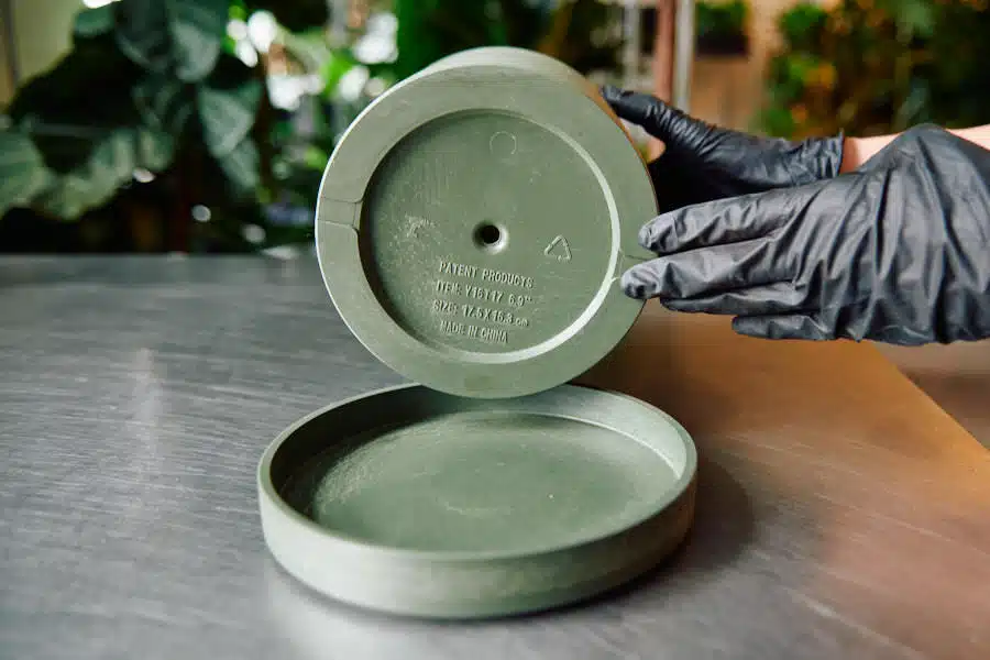 Close-up of hands wearing black gloves holding a green planter pot with drainage holes, demonstrating the importance of proper pot selection for ZZ plant repotting.